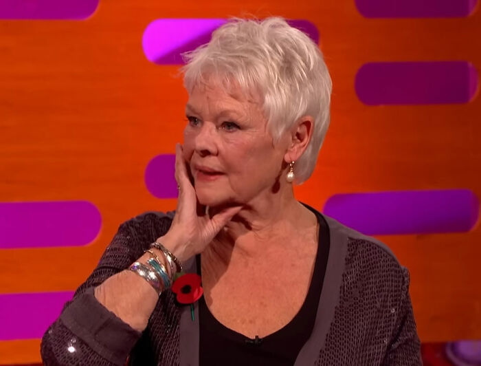 Dame Judi Dench on a colorful talk show set, sharing a heartfelt health confession with a thoughtful expression.