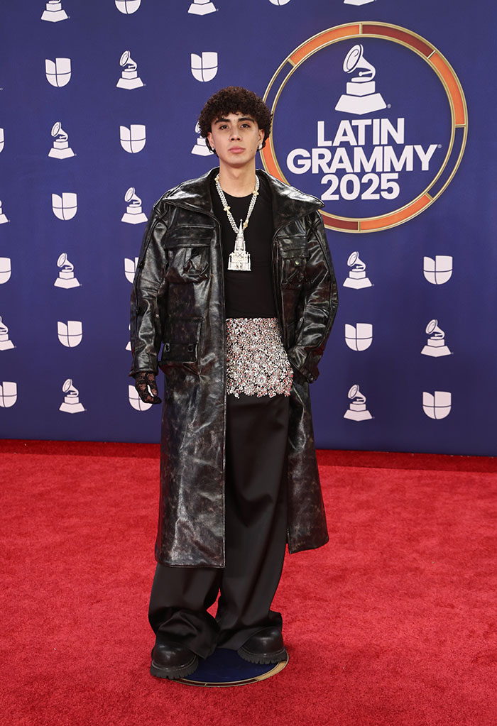 Young male star at 2025 Latin Grammy Awards wearing oversized leather coat and embellished outfit on the red carpet.