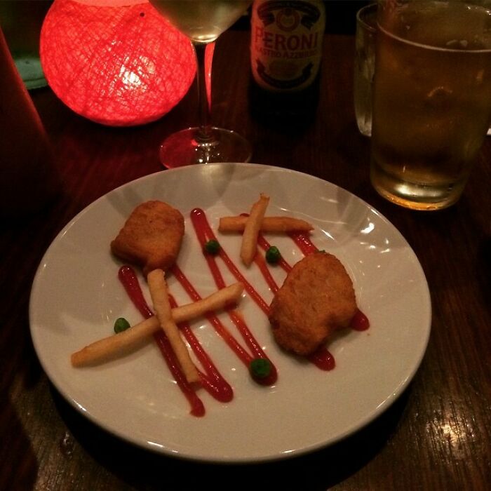 Plate with chicken nuggets, fries, and peas arranged on ketchup lines, illustrating men never grow up playful food art.