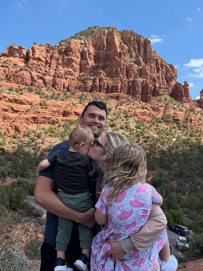 Family embracing outdoors by red rock cliffs, illustrating emotional exchange as revealed by lip reader at TPUSA event.