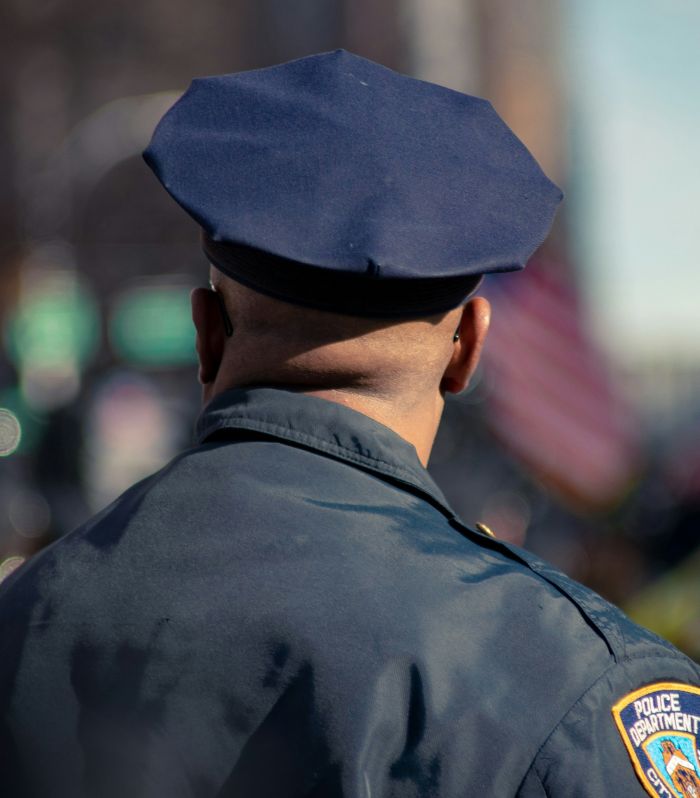 Police officer from behind wearing uniform and cap, involved in investigation of woman found chained in backyard case.