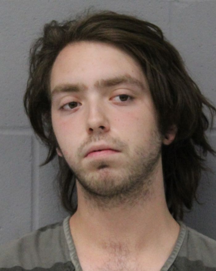 Mugshot of a young man with unkempt hair and a somber expression linked to woman found chained in backyard case.