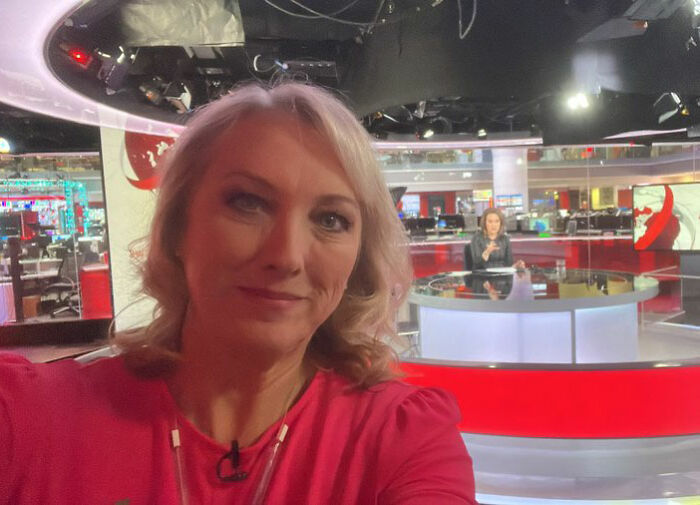 BBC anchor in newsroom wearing red, related to controversy over showing disgust on-air in remark about trans people.