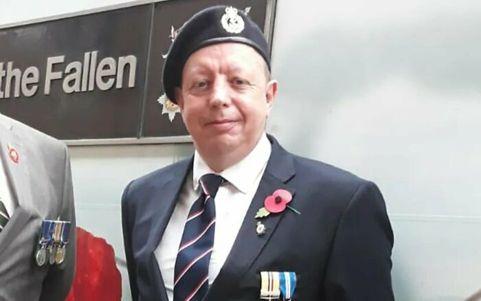 Man in military uniform wearing medals and a poppy, honored as hero old man who blocked knife attack on girl during UK train rampage.