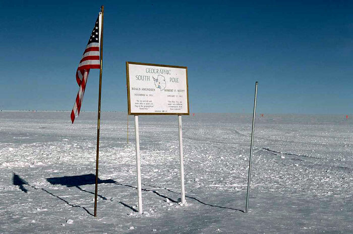 Remote location at the Geographic South Pole, featuring an American flag and a sign in a vast icy landscape.