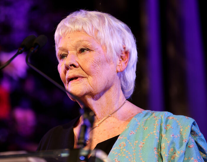 Dame Judi Dench speaking at an event, illuminated by stage lighting, sharing a heartfelt health confession.