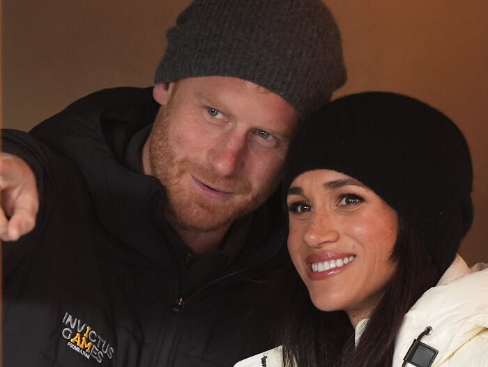 Prince Harry and Meghan Markle wearing winter hats, smiling closely during a casual outdoor moment at home.