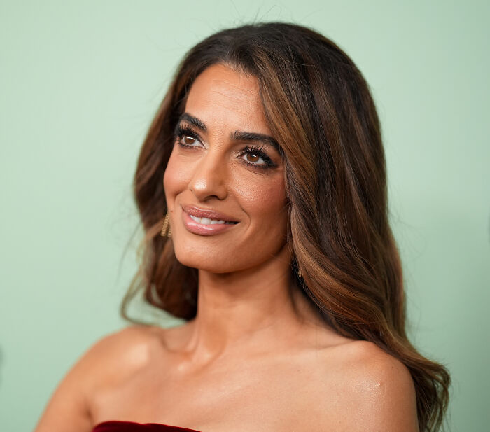 Amal Clooney posing in a red dress with natural makeup and styled hair after a major Photoshop blunder controversy.