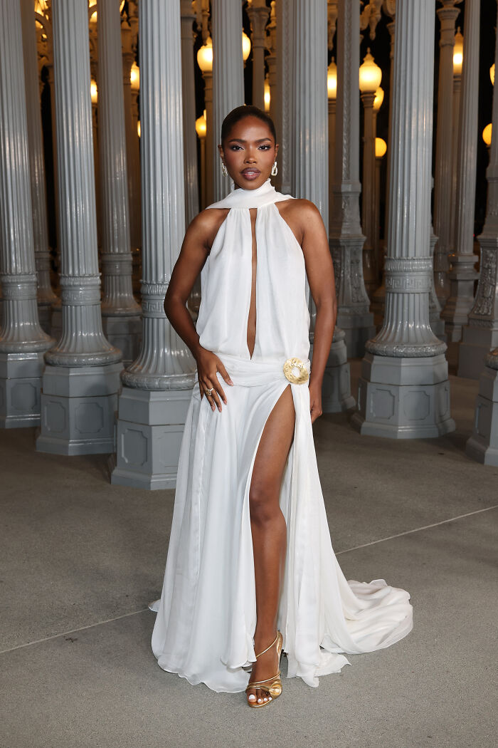 Woman in a white flowing gown with high slit and gold details, posing at the 2025 LACMA Art and Film Gala outfits event.