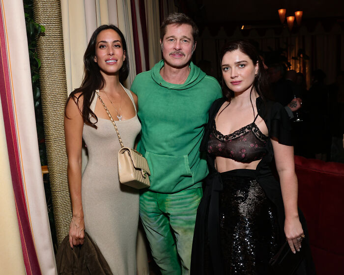 Brad Pitt at Hollywood premiere with two women, wearing a green hoodie, sparking speculation about his appearance.