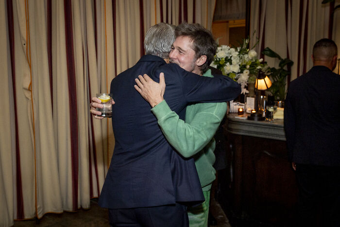 Brad Pitt wearing a green outfit hugging a man in a dark suit at a Hollywood premiere event.