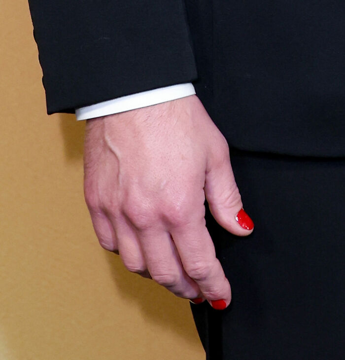 Close-up of a man's hand in a suit with red nail polish, highlighting a unique detail in a perfect man look.