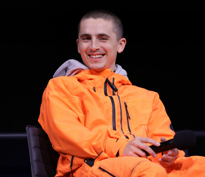 Timothée Chalamet smiling in bright orange jacket during a panel, reflecting on going into psychosis moments. Timothée Chalamet smiling in bright orange jacket during a panel, reflecting on going into psychosis moments.