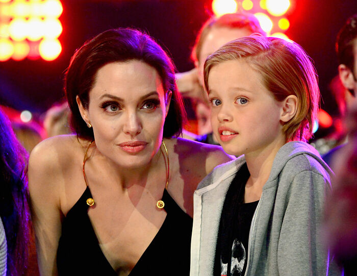 Angelina Jolie with son Knox, 17, showing his bold new look at a lively event with bright lights in the background.