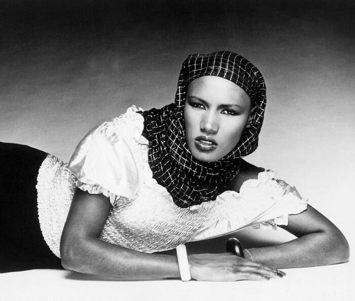Black and white photo of a style icon wearing a patterned headscarf and vintage textured blouse, shaping fashion trends.