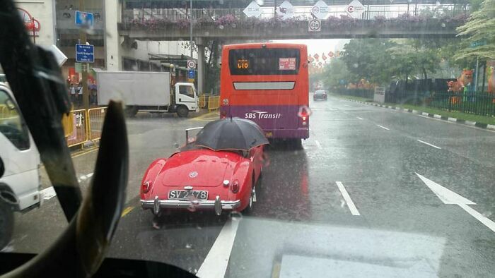 Vintage red car with an umbrella on a rainy street, showcasing people with zero common sense in traffic.