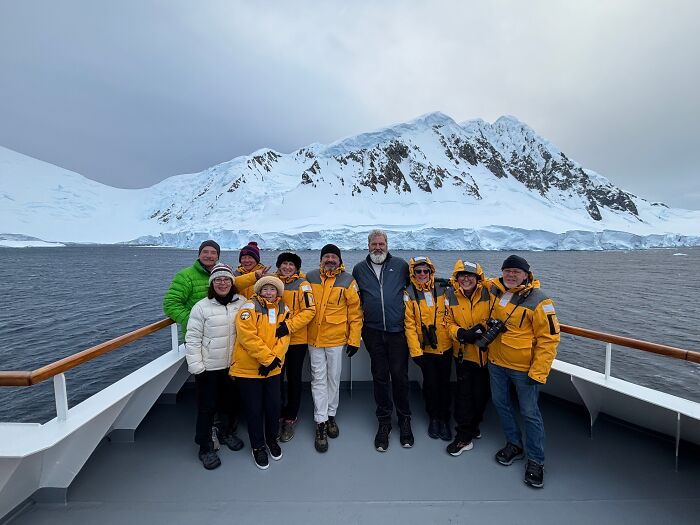 Group of travelers in yellow jackets on a ship with stunning Antarctica snow-covered mountains and icy waters in the background. Group of travelers in yellow jackets on a ship with stunning Antarctica snow-covered mountains and icy waters in the background.