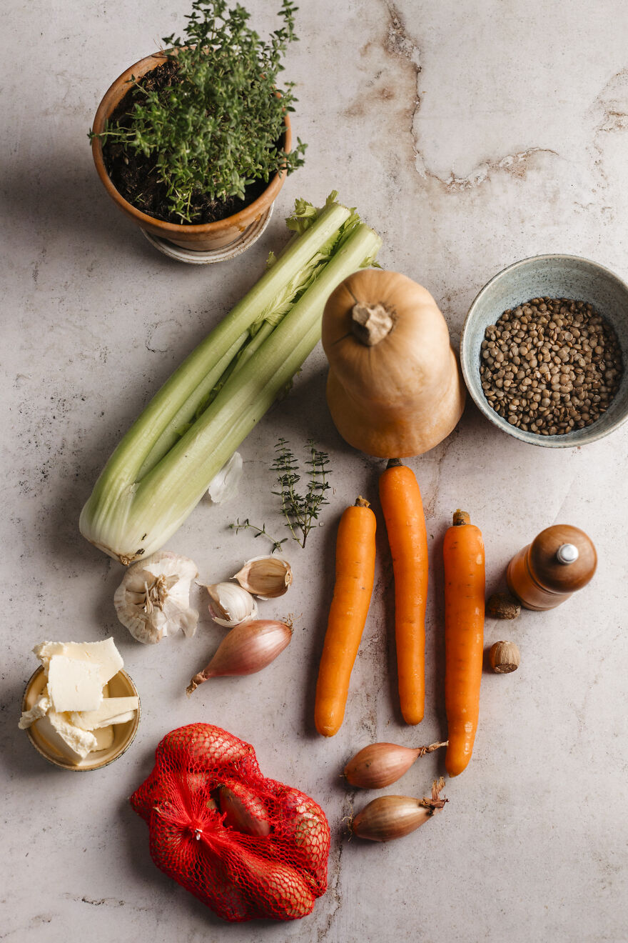 Autumn pie ingredients including carrots, celery, shallots, garlic, butternut squash, lentils, butter, and fresh herbs on a stone surface.