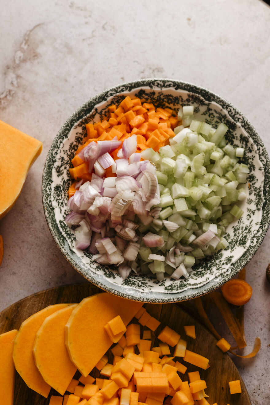 Diced butternut squash, shallots, and celery in a bowl, key ingredients for a go-to autumn pie recipe.