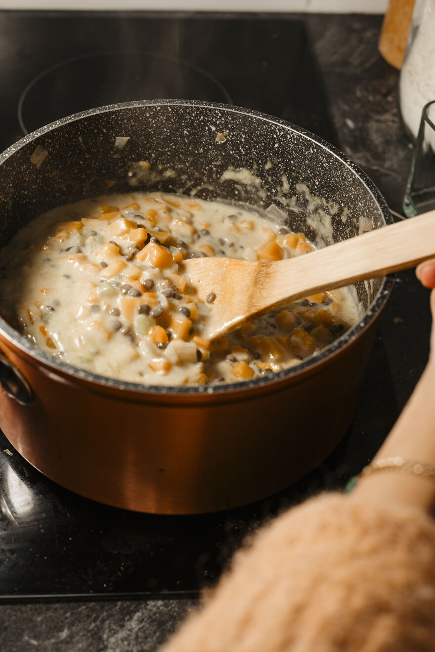 Autumn pie recipe filling cooking in a pot with vegetables and creamy sauce being stirred with a wooden spoon.