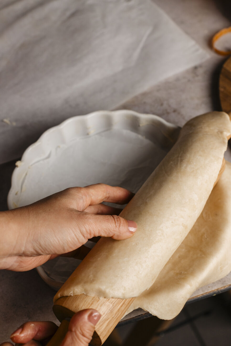 Hands rolling autumn pie crust dough over a pie dish, preparing a go-to autumn pie recipe at home.
