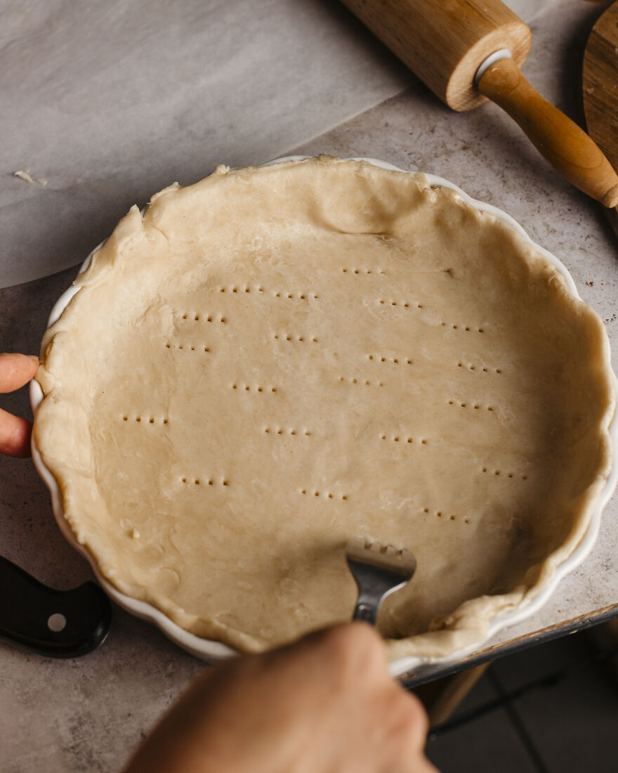 Hands preparing an autumn pie crust in a baking dish, ideal for juggling motherhood and busy deadlines.