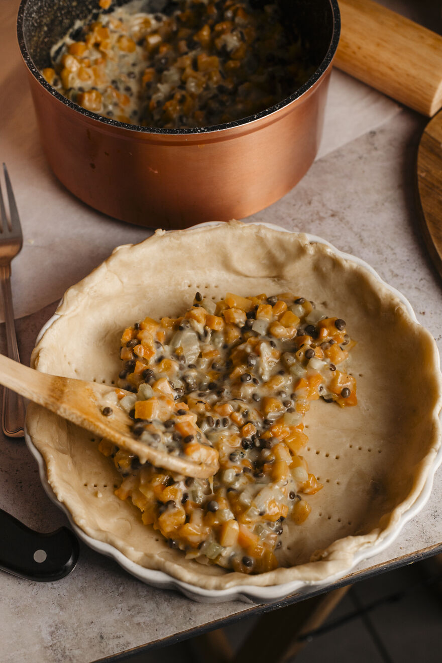 Autumn pie recipe filling with vegetables being spooned into crust, perfect for busy moms managing deadlines.