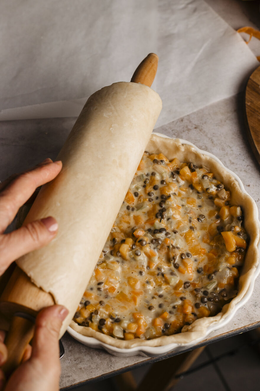 Rolling pie crust over autumn pie filling with lentils and vegetables, perfect for a warm autumn pie recipe.
