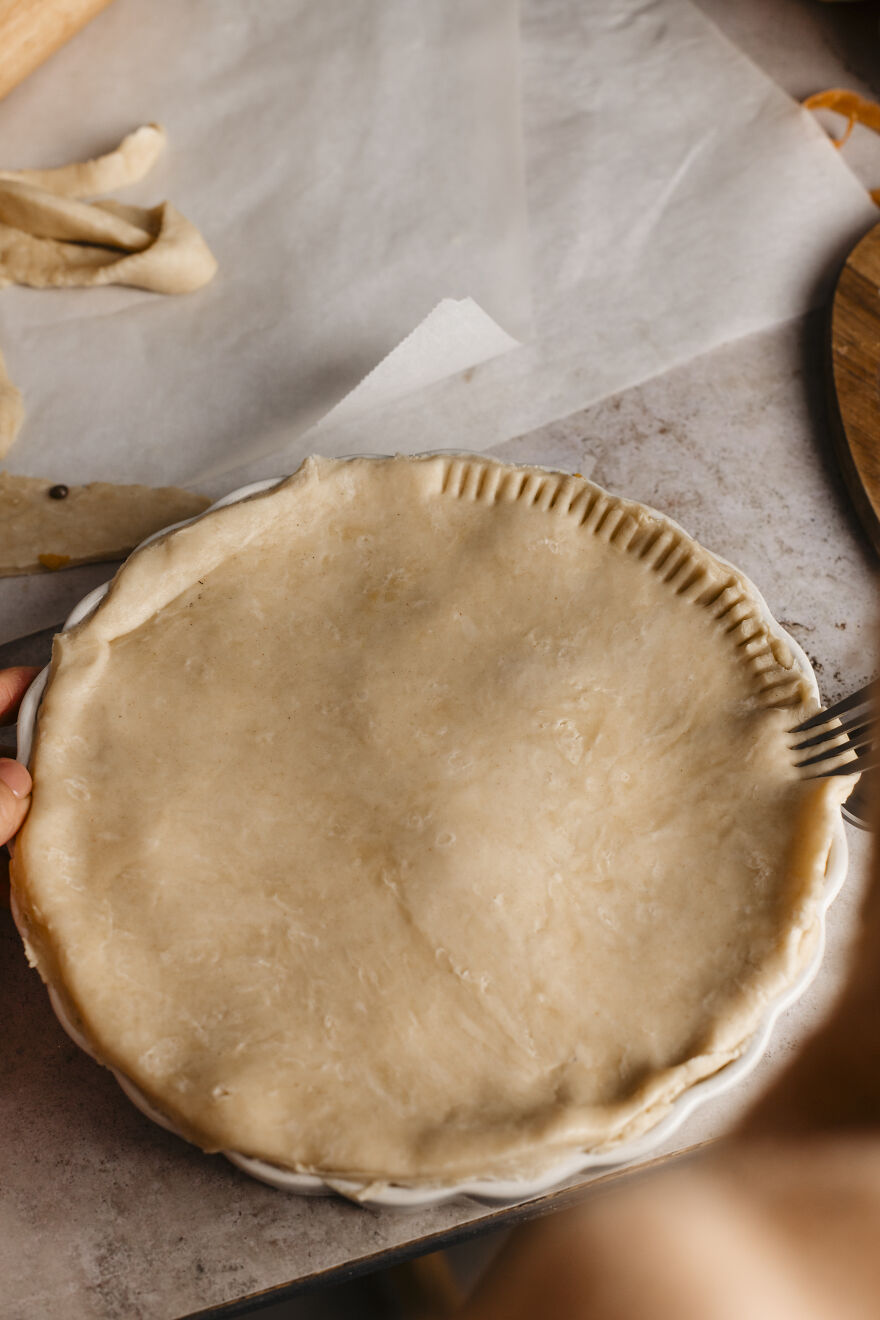 Unbaked autumn pie crust being prepared and crimped by hand, ready for baking and cozy seasonal warmth.