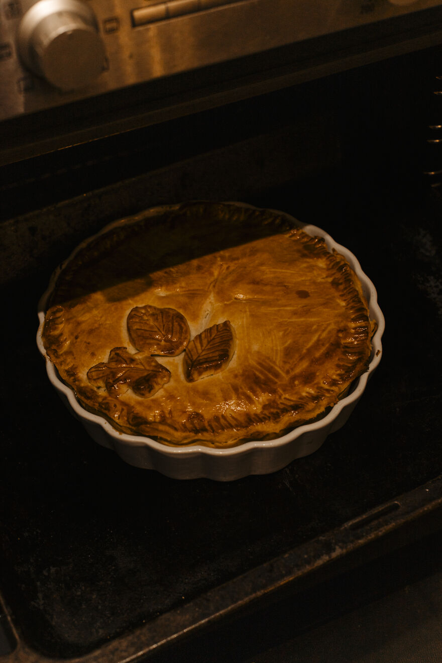 Golden autumn pie baking in an oven, showing a warm crust with decorative leaf patterns in a round dish.