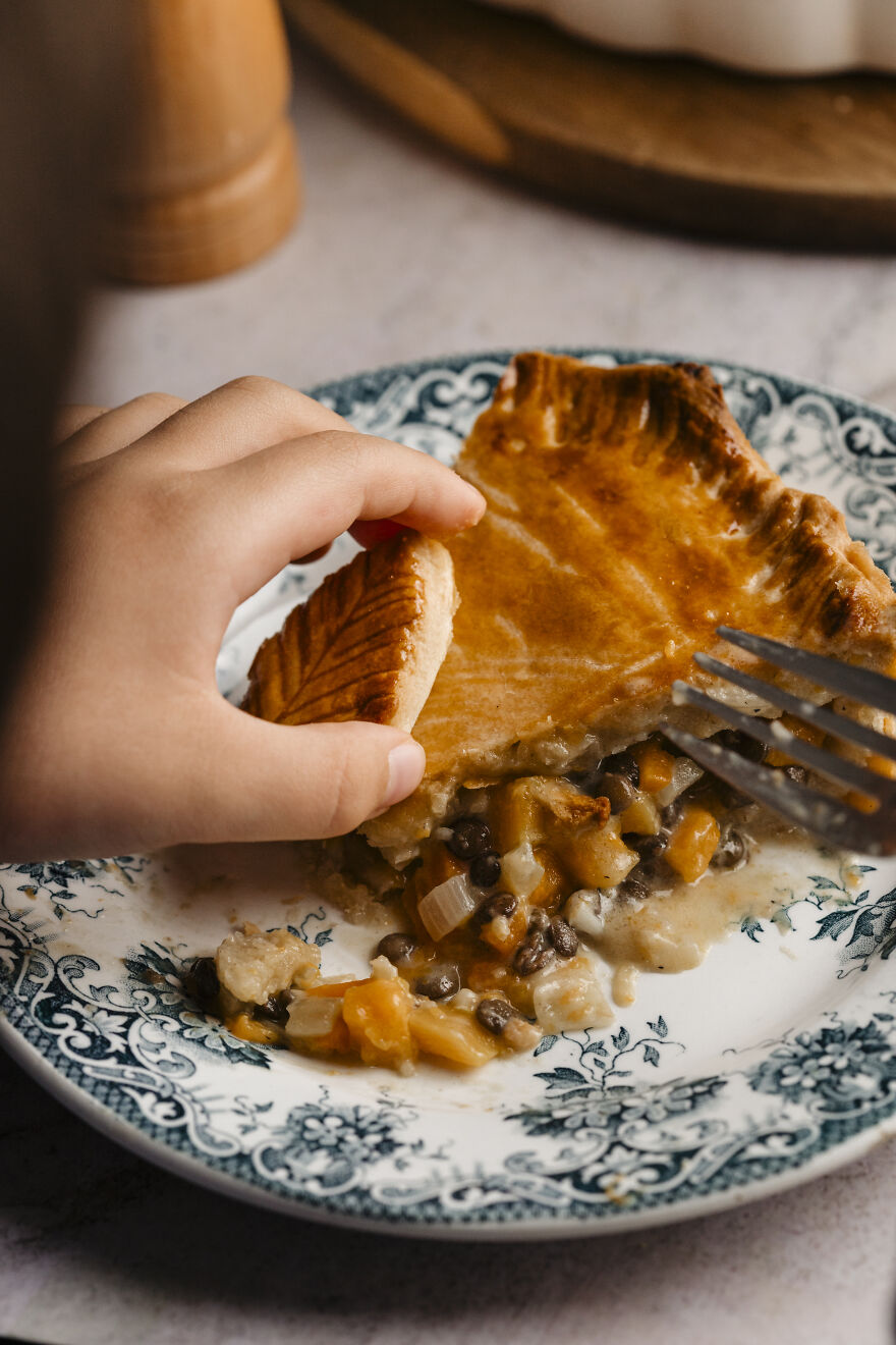 Hand holding a slice of autumn pie with vegetable filling on a decorative plate, showcasing a cozy seasonal recipe.