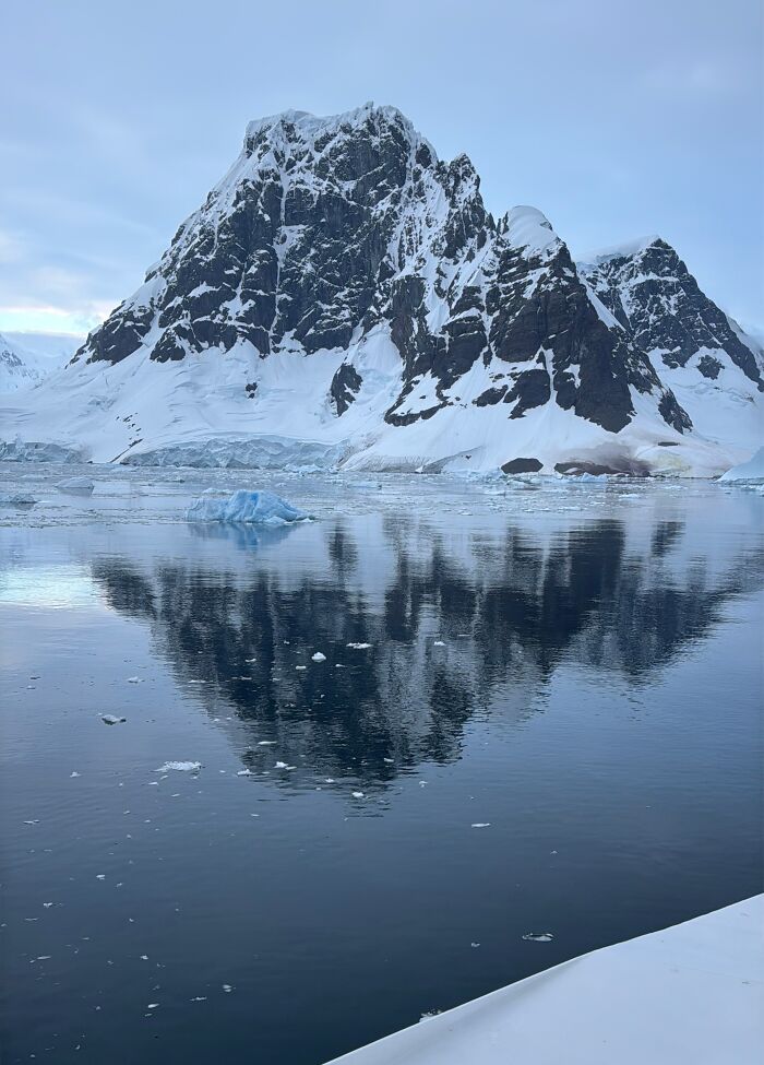 Snow-covered Antarctic mountain reflecting in calm icy waters, showcasing the scale and beauty of Antarctica adventure. Snow-covered Antarctic mountain reflecting in calm icy waters, showcasing the scale and beauty of Antarctica adventure.