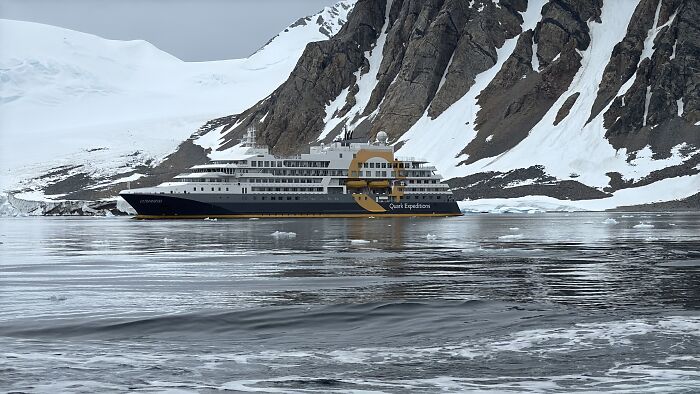 Expedition cruise ship navigating icy Antarctic waters with towering snow-covered mountains in the background. Expedition cruise ship navigating icy Antarctic waters with towering snow-covered mountains in the background.