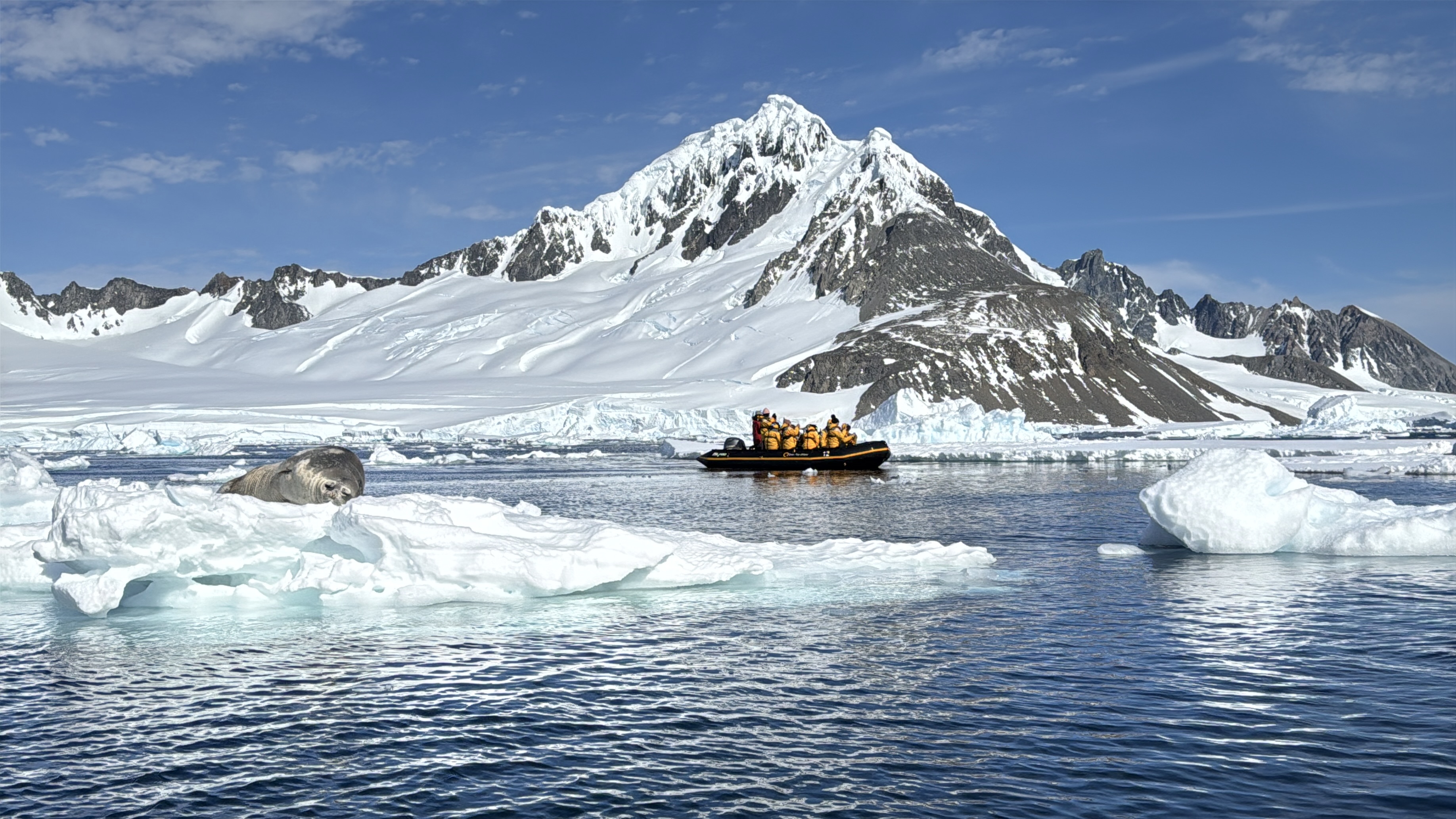 Tourists in a boat exploring the scale and beauty of Antarctica with snow-covered mountains and a seal on icebergs. Tourists in a boat exploring the scale and beauty of Antarctica with snow-covered mountains and a seal on icebergs.