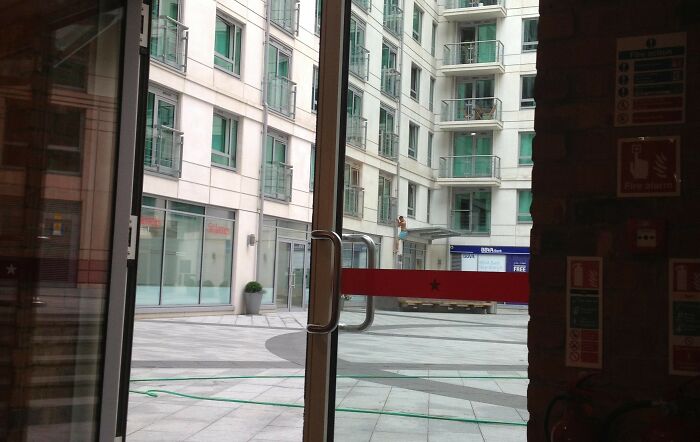 View through glass doors showing modern apartment complex courtyard with reflections and urban architecture details in daylight