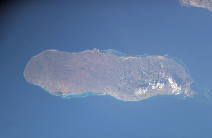 Aerial view of a remote foreign island surrounded by blue ocean waters and clear skies.