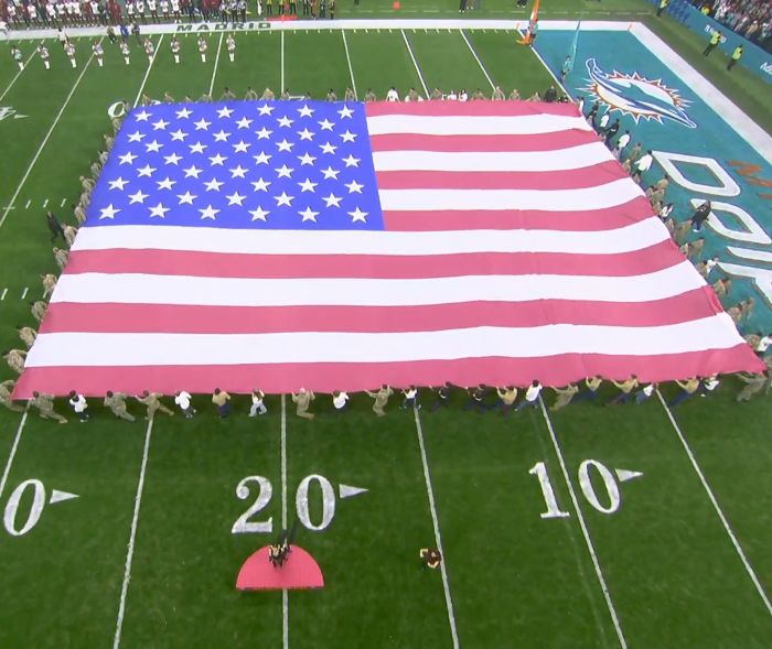 Large American flag displayed on NFL field during US national anthem as singer faces backlash for inappropriate outfit.