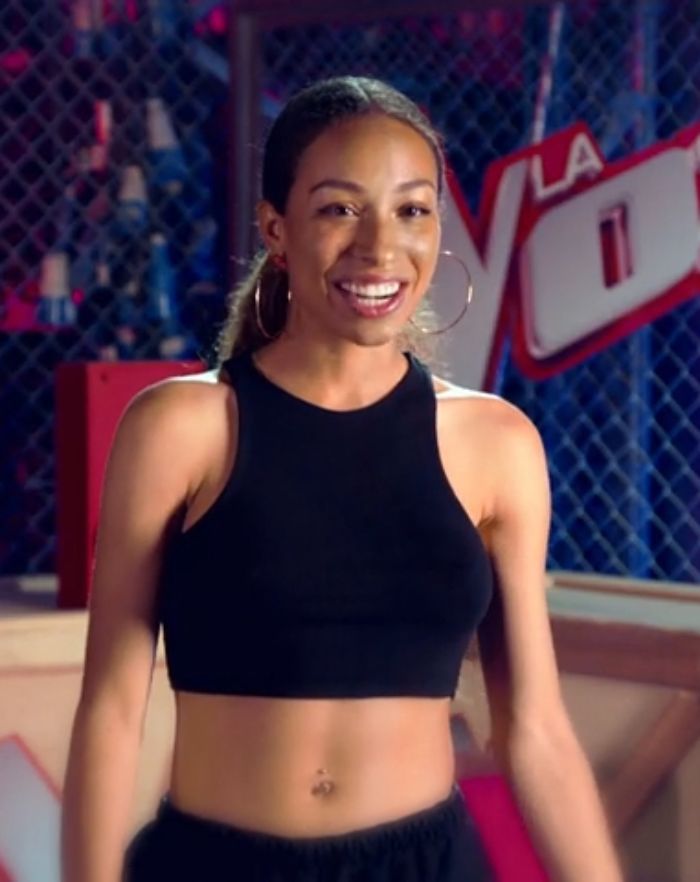Young singer in a black crop top smiling, debated for wearing an inappropriate outfit during US national anthem at NFL game.