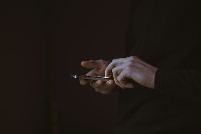 Person in dark clothing holding and using a smartphone, reflecting on not forgiving brother after mom’s passing news. Person in dark clothing holding and using a smartphone, reflecting on not forgiving brother after mom’s passing news.