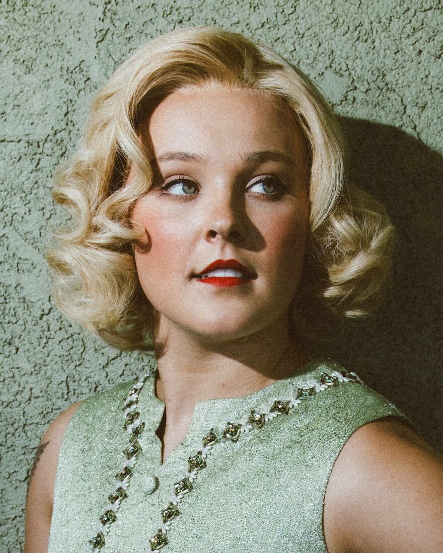 Jojo Siwa with vintage hairstyle and green embellished dress posing against textured wall, highlighting music streams and merch sales. Jojo Siwa with vintage hairstyle and green embellished dress posing against textured wall, highlighting music streams and merch sales.