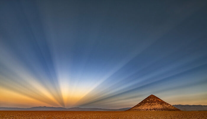 Desert landscape with a solitary mountain under colorful rays of light showcasing nature's award-winning beauty.
