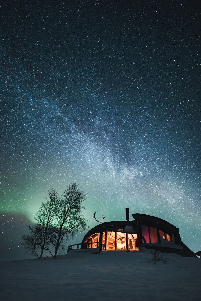 Cozy cabin under a starry sky with faint northern lights visible, showcasing the best places and times to see the Northern Lights.