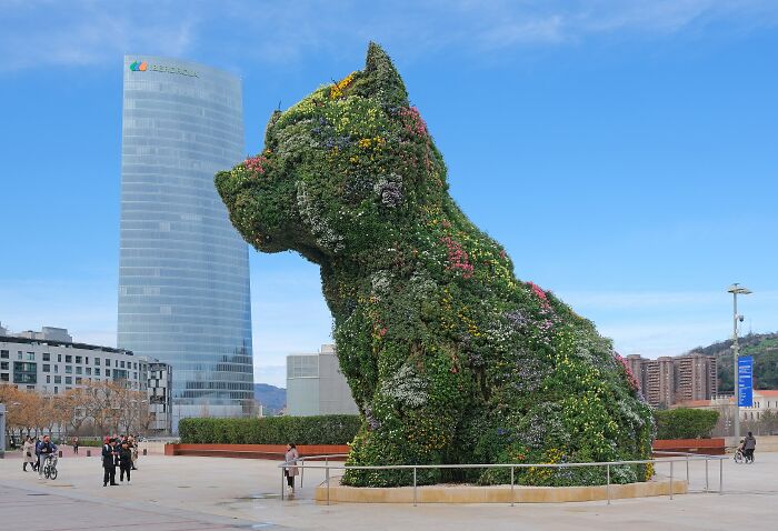 Giant floral sculpture of a dog in an urban plaza, showcasing one of the spectacular sculptures across the globe.