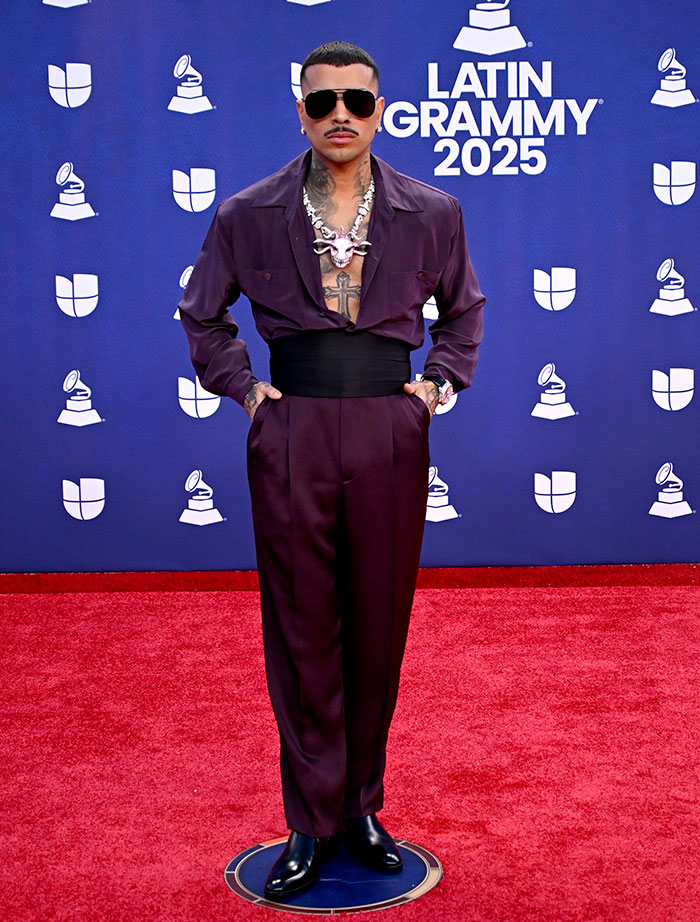 Man wearing an unconventional outfit with a large necklace and sunglasses at the 2025 Latin Grammy Awards red carpet.