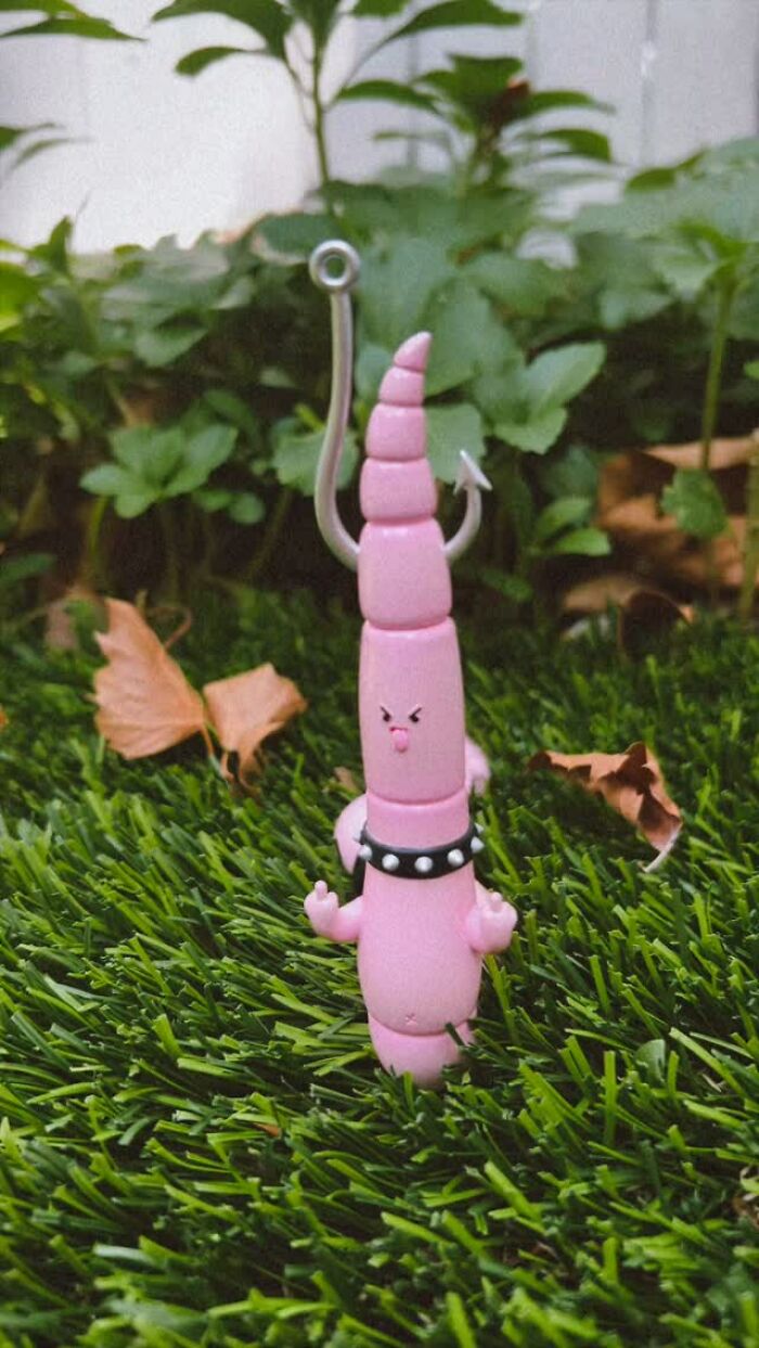 Pink quirky sculpture with personality in grass, featuring expressive face and spiked collar, part of artist made collection.