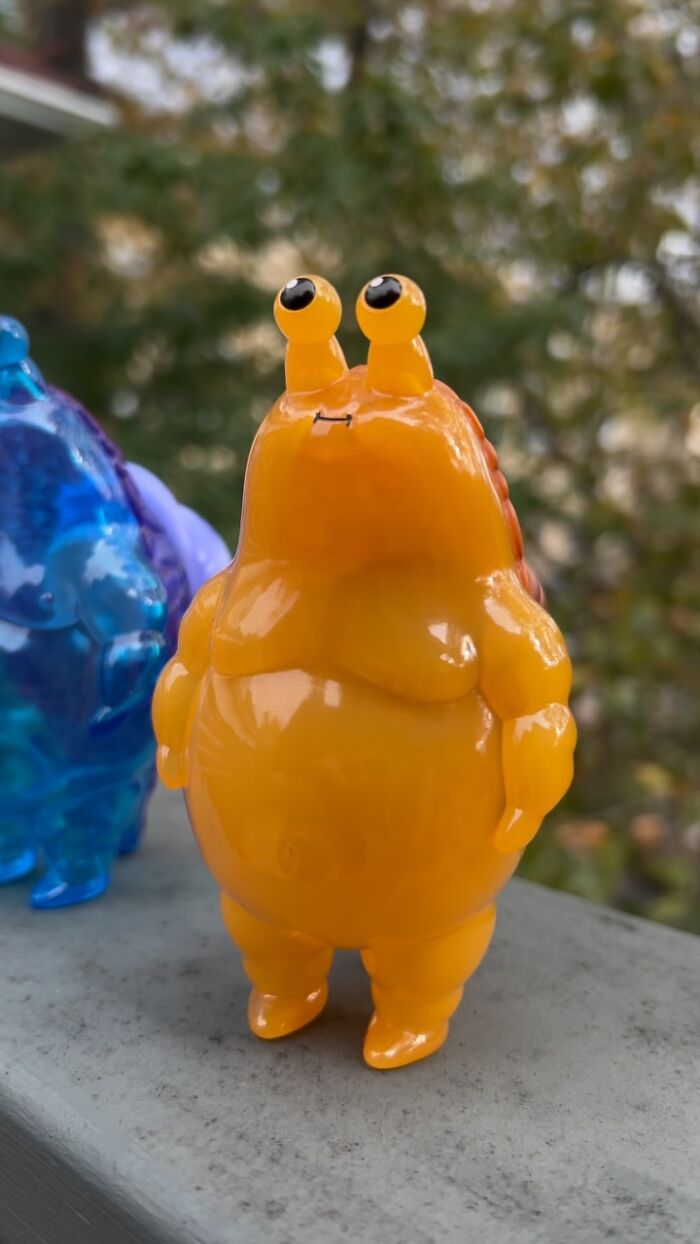 Glossy orange quirky sculpture with bulging eyes and an expressive face, showcasing unique personality and artistic charm outdoors.