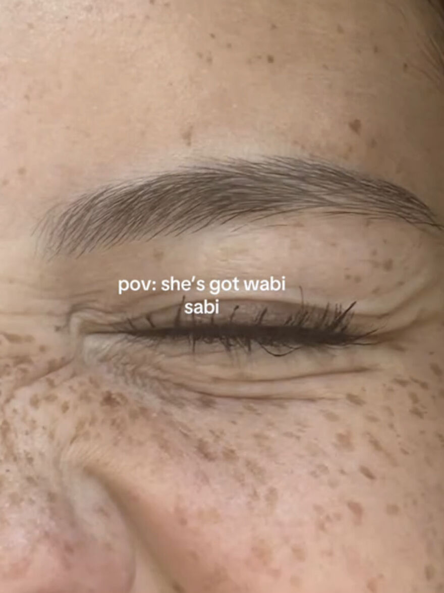 Close-up of a smiling eye with freckles and wrinkles, showcasing perfect imperfections in a wholesome trend.