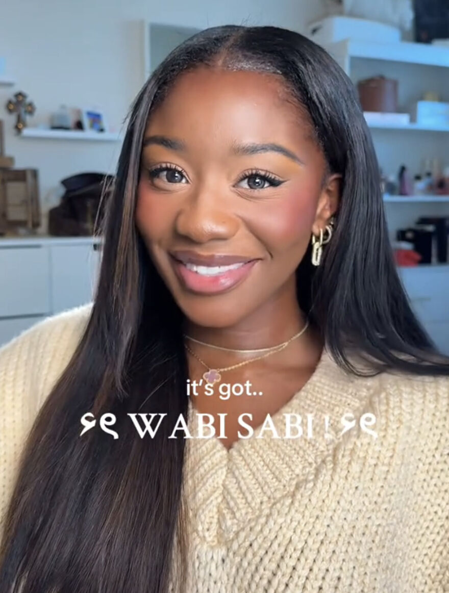 Smiling woman with long hair and gold earrings, embracing perfect imperfections in a wholesome trend about self-acceptance.