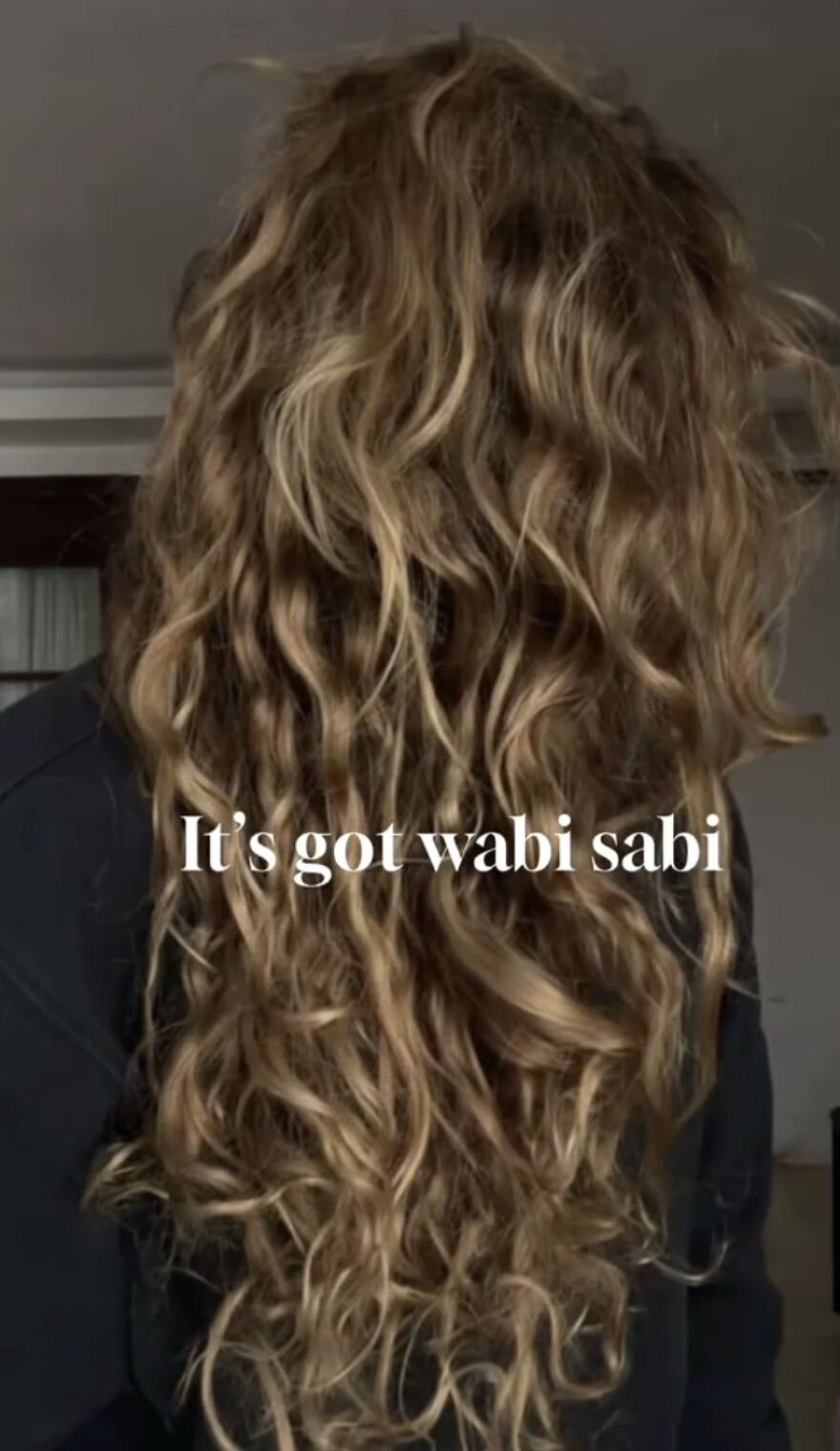Person with long, curly hair embracing perfect imperfections, showcasing the beauty of the wholesome trend of self-acceptance.