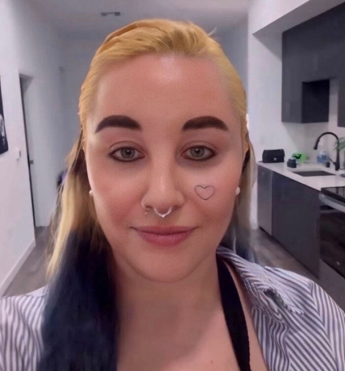Amanda Bynes with septum piercing and heart tattoo on cheek, posing indoors amid viral claim involving Dan Schneider.
